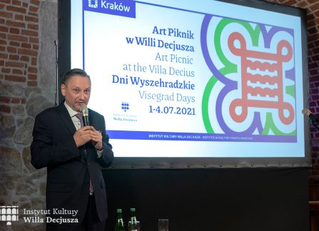 fotografia. projekcja filmu w ramach festiwalu art piknik w willi decjusza. Jarosław Krykwiński, Konsul Honorowego Republiki Czeskiej w Częstochowie wygłasza wprowadzenie do filmu. w tle grafika promująca festiwal.